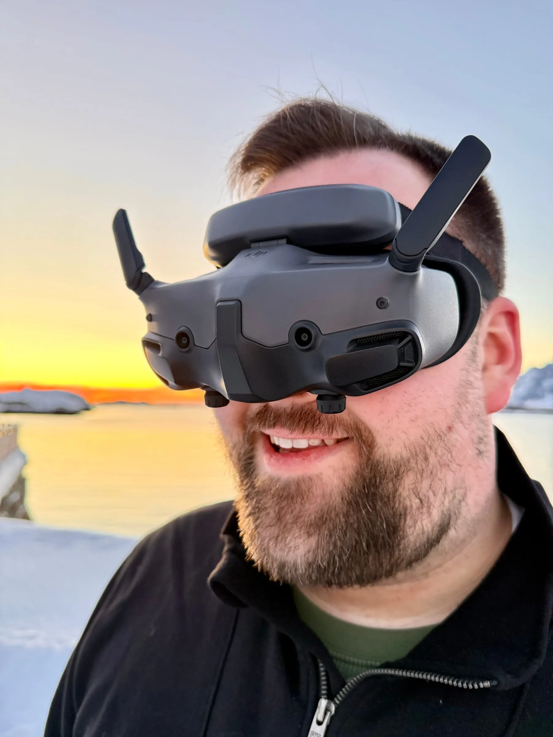 André Meschkat mit einer FPV-Videobrille auf dem Kopf, im Hintergrund eine verschneite Küste bei Sonnenuntergang